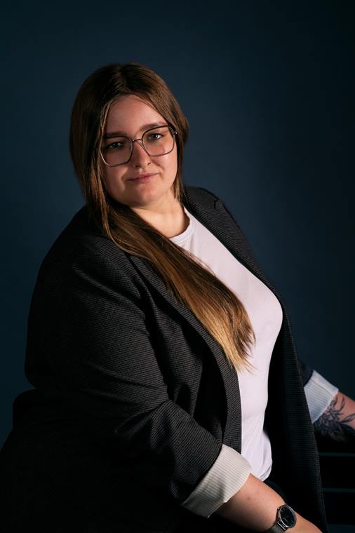 Frau im Blazer sitzt vor dunkelblauem Hintergrund