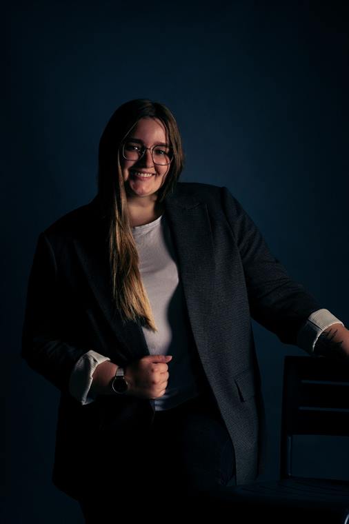 Frau im Blazer lehnt an einem Stuhl