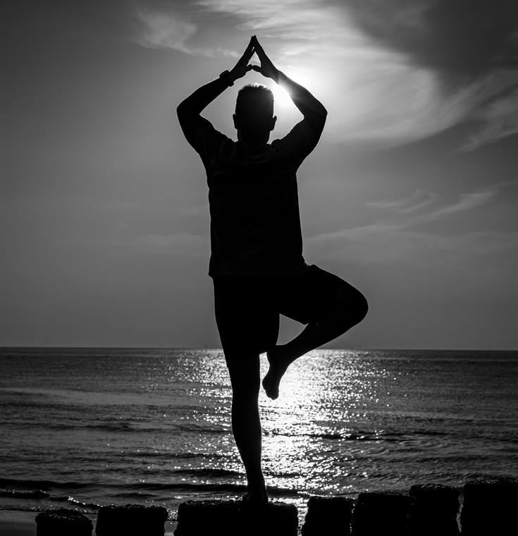 Silhouette in Yogapose am Meer im Gegenlicht