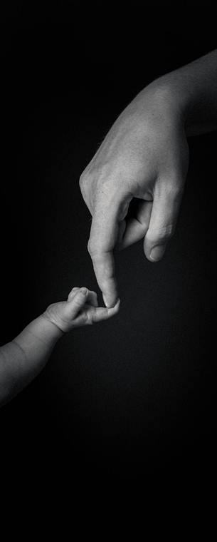 Babyhand greift nach einem Finger, schwarzer Hintergrund