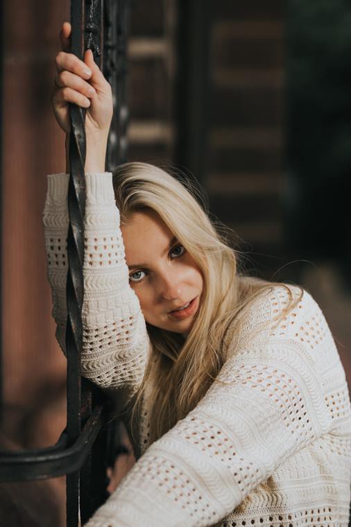 Blonde Frau lehnt an einem eisernen Tor
