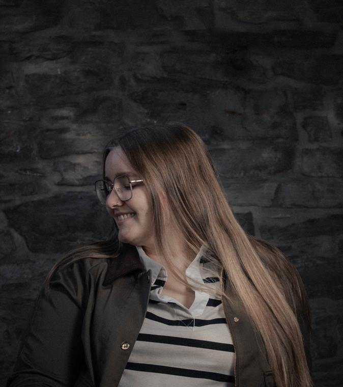 Frau mit Brille vor einer Steinmauer