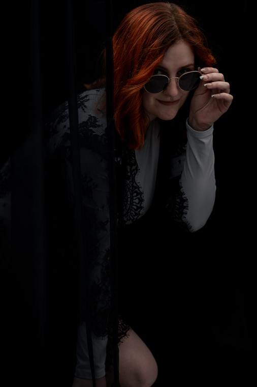 Frau mit roten Haaren und Sonnenbrille im dunklen Studio
